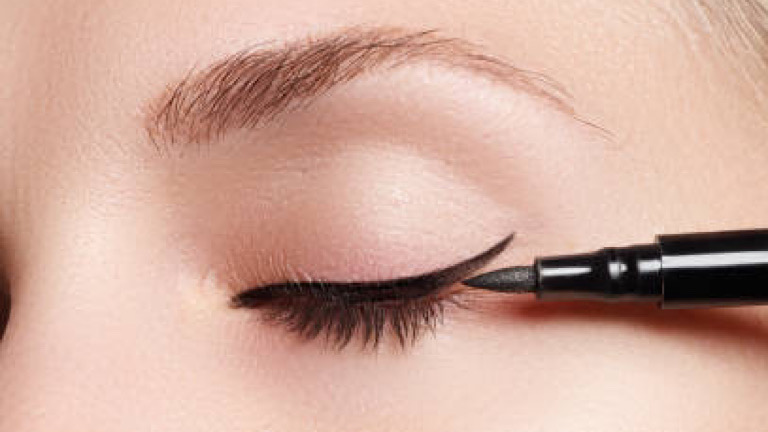 Beautiful model applying eyeliner close-up on eye